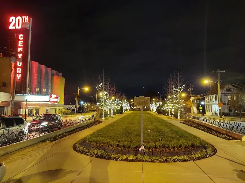 20th Century Theater neon sign lit up at night beside the tree-lined median of Oakley Square
