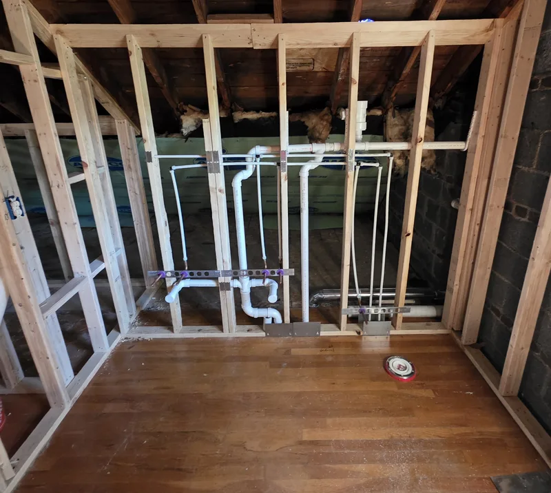Attic bathroom rough-in with white PEX supply lines and PVC drains in new stud framing over a wood floor