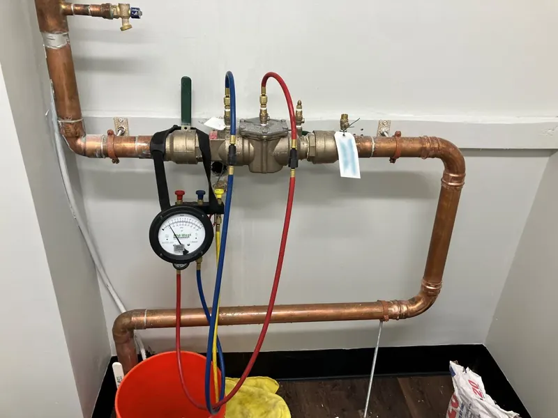 Backflow preventer on a copper loop being tested, with a test kit gauge connected by red, blue and yellow hoses