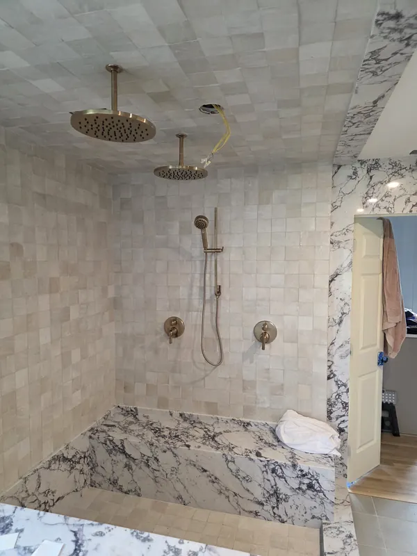 Brushed brass rain shower head, handheld shower and valve trim in a tiled shower