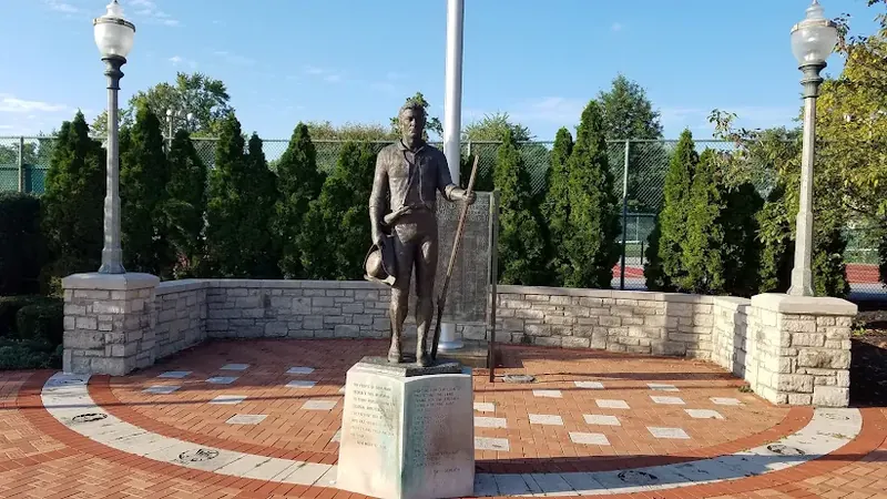 Bronze statue of a man in a hat holding a rifle in a brick plaza in Deer Park