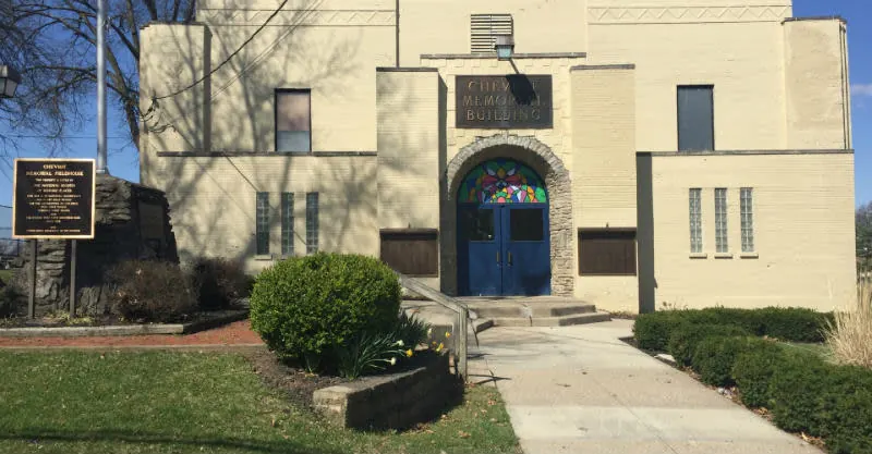 Cheviot Memorial Building, a cream brick fieldhouse with blue double doors under a stained-glass arch