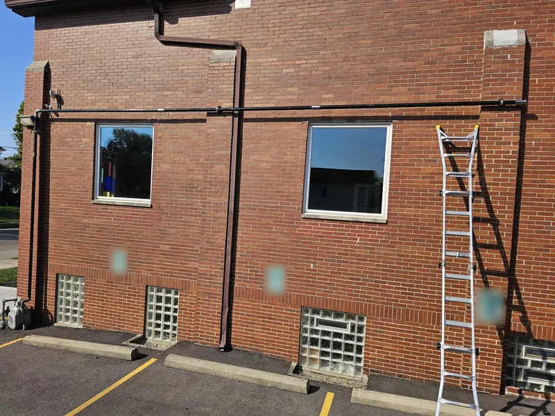 Black steel gas line run along the brick wall of a church, with a ladder set up for the work