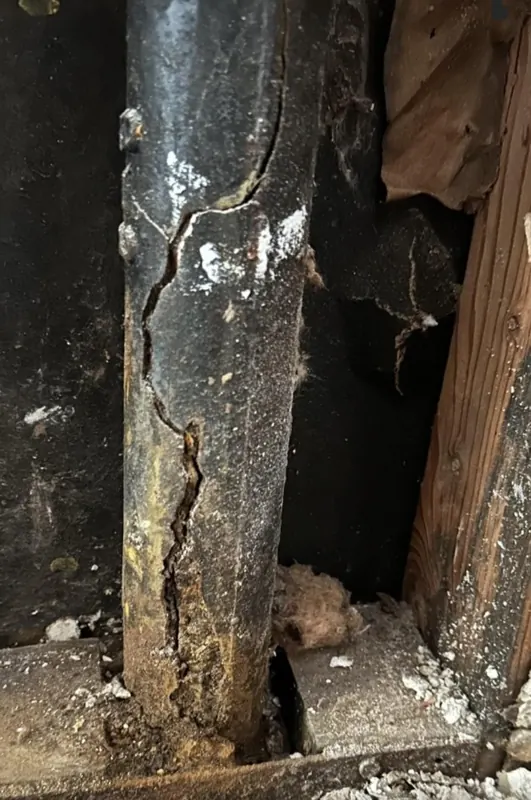 Vertical cast-iron drain stack with long cracks and corrosion at the base
