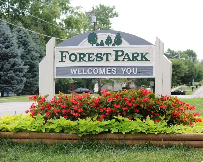 Forest Park Welcomes You sign behind a bed of red flowers