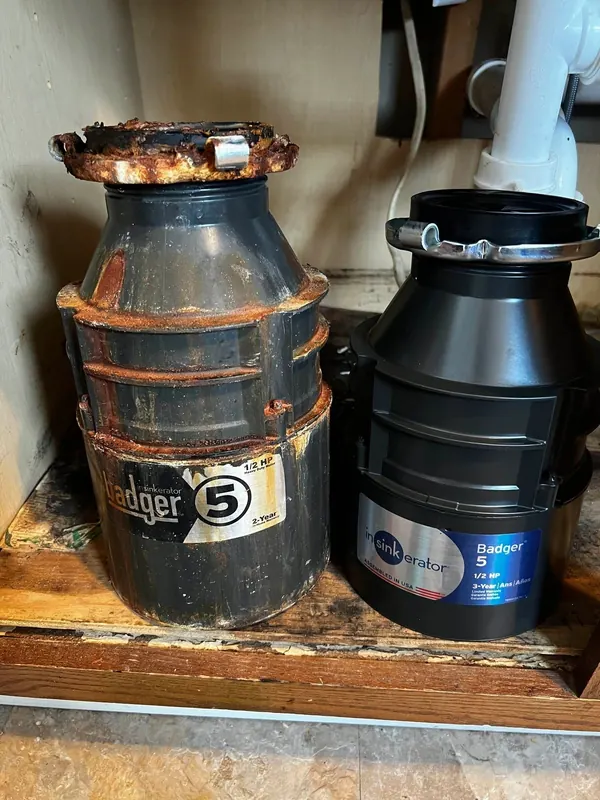 Old rusted InSinkErator Badger 5 garbage disposal next to the new Badger 5 that replaced it under a kitchen sink