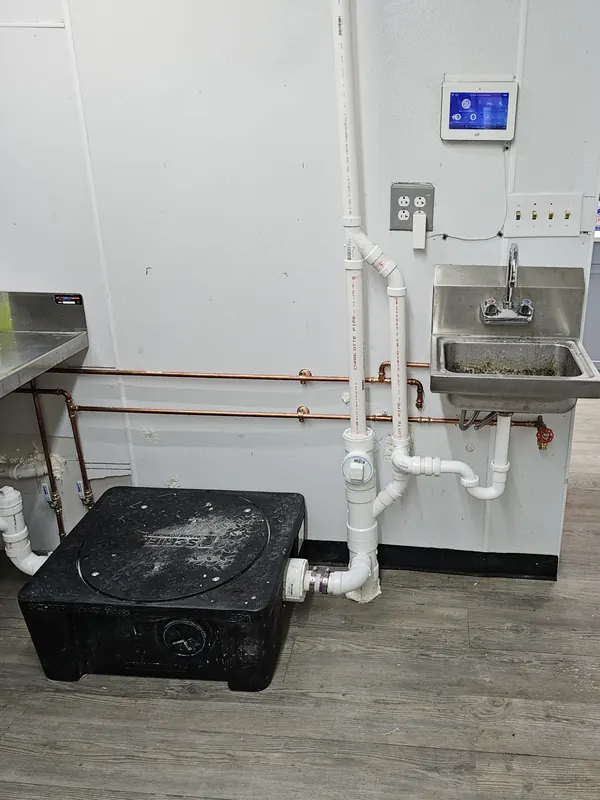 Floor grease interceptor with new PVC drain piping beside a wall-mounted hand sink
