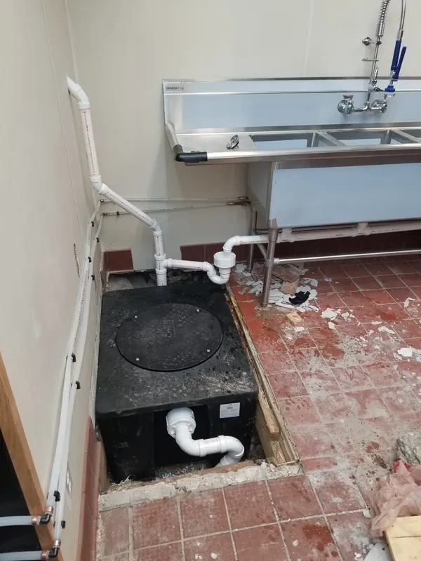 Grease interceptor connected below a stainless three-compartment sink