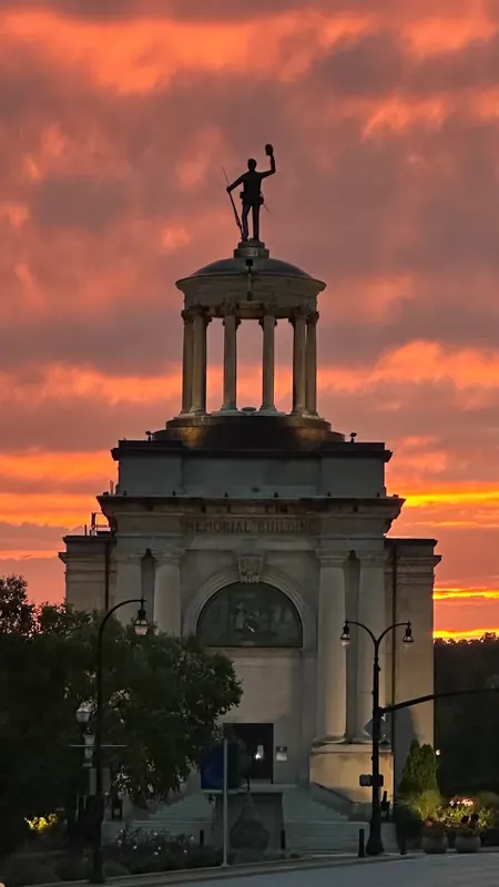 Hamilton Memorial Building topped by a statue, silhouetted against an orange sunset sky