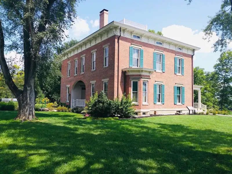 Historic two-story brick house with green shutters on a lawn in Trenton