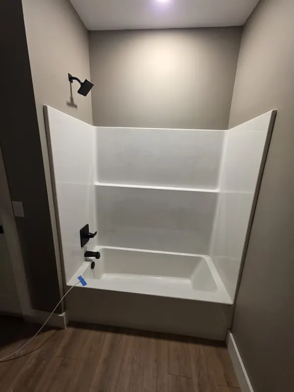 New bathtub and shower surround with black tub spout, valve trim and showerhead plumbed during a bathroom remodel