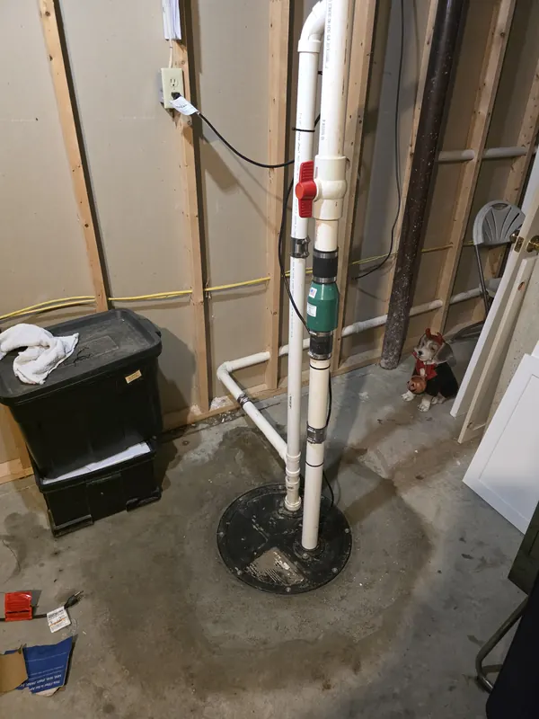 New sewage ejector pump basin with white PVC discharge pipe, red ball valve and green check valve in a basement