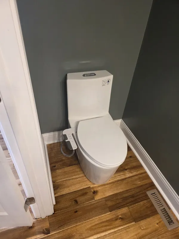 New one-piece toilet with a bidet seat installed in a half bath with a wood floor