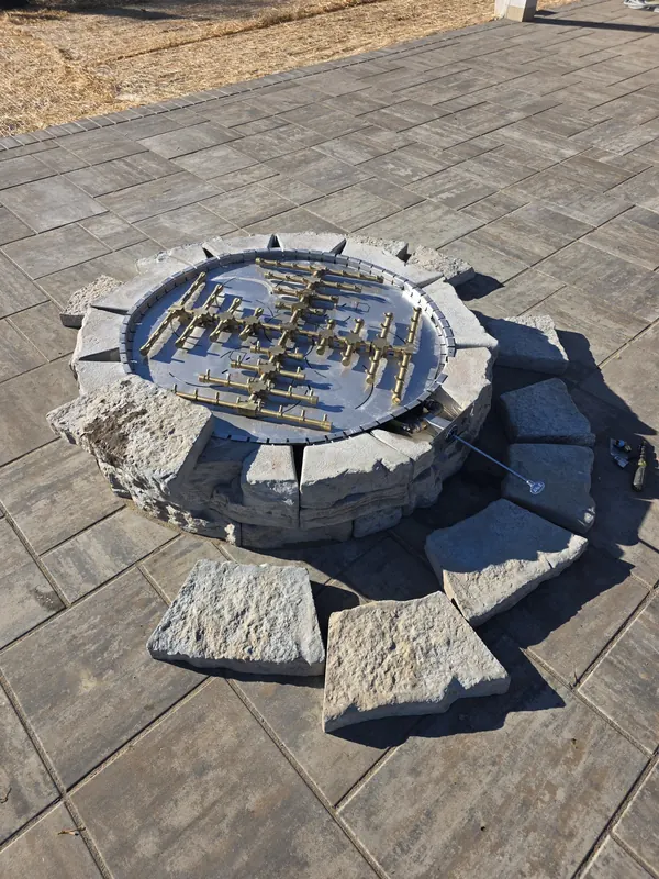Gas burner installed in a stone fire pit on a paver patio, connected to a new outdoor fireplace gas line