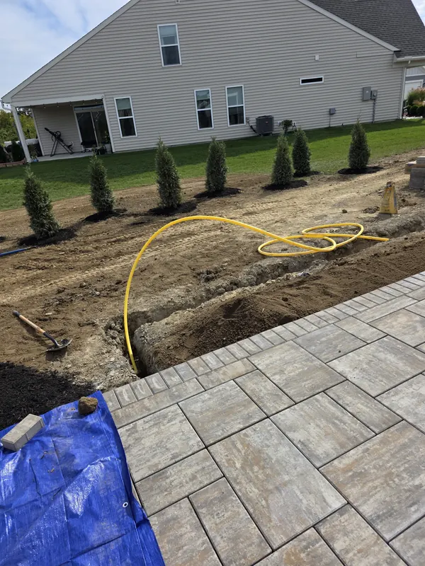 Yellow gas line laid in a trench beside a paver patio for an outdoor fireplace