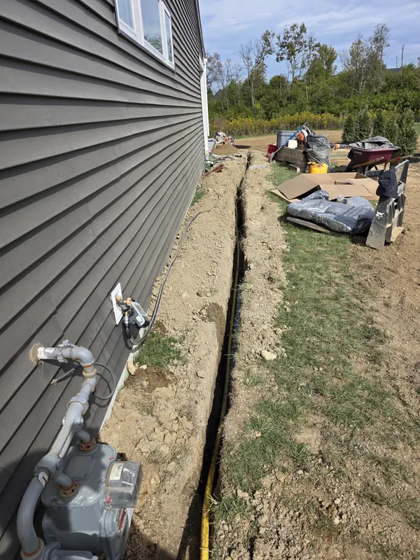 Yellow gas line laid in a trench along the side of a house, running from the gas meter to an outdoor fireplace