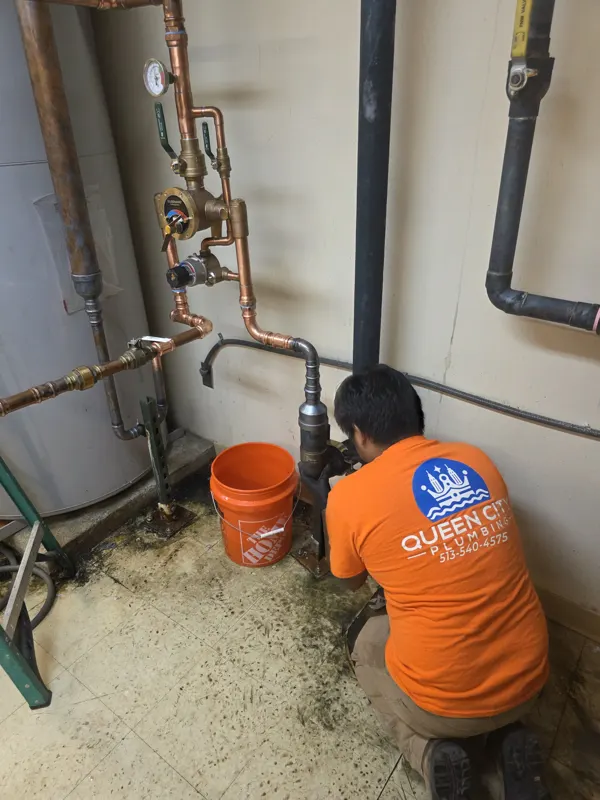 Queen City Plumbing plumber in a company shirt working on piping at floor level
