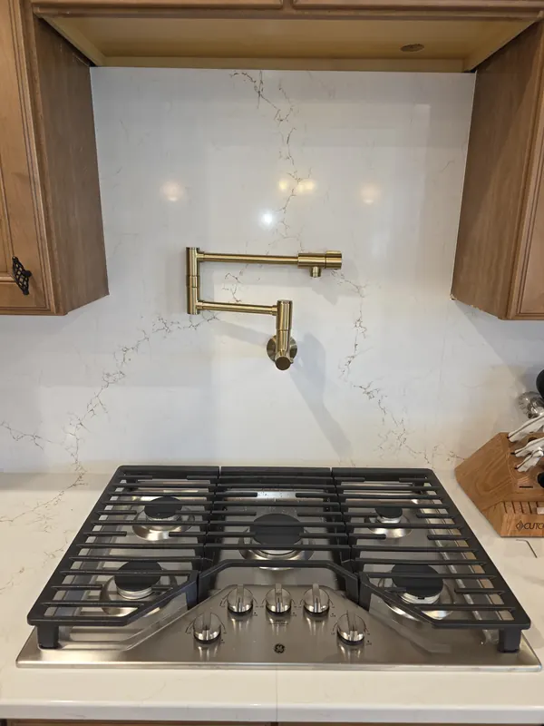 Brass wall-mounted pot filler faucet over a gas cooktop