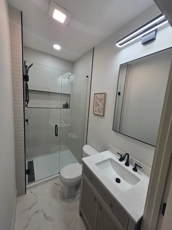 Finished bathroom with a glass shower, toilet and vanity sink after remodel plumbing
