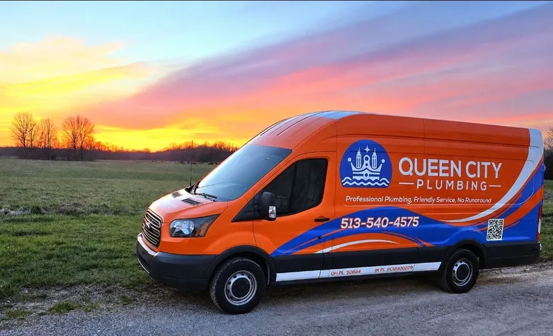 Queen City Plumbing orange service van with 513-540-4575 and license numbers on the side, parked by a field at sunset