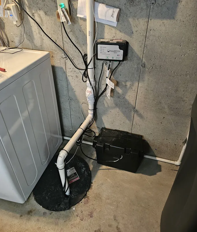 Sump pump basin with PVC discharge line and pump controller in a basement