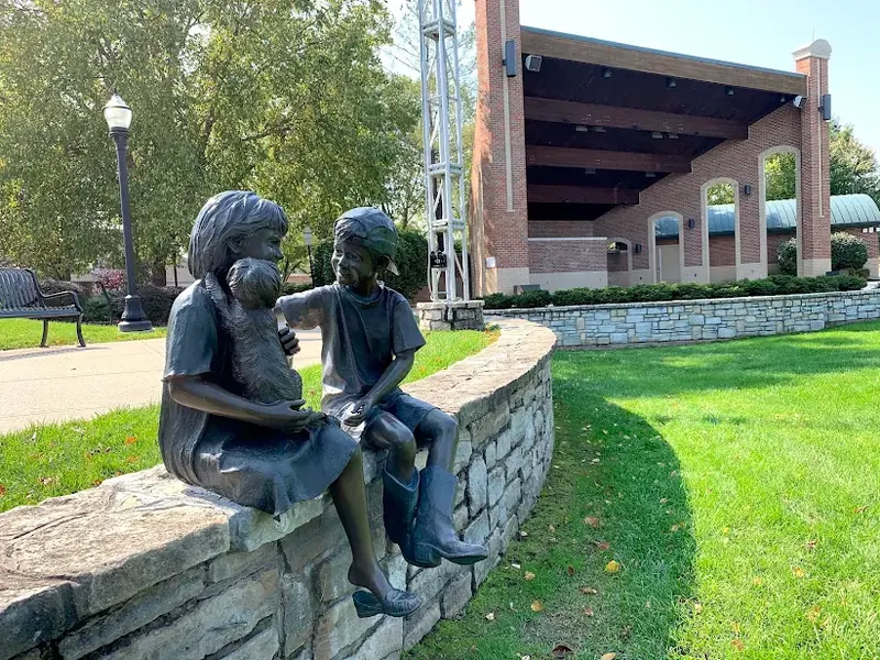 Bronze statue of two children and a dog on a stone wall in front of the Village Green amphitheater in Fairfield