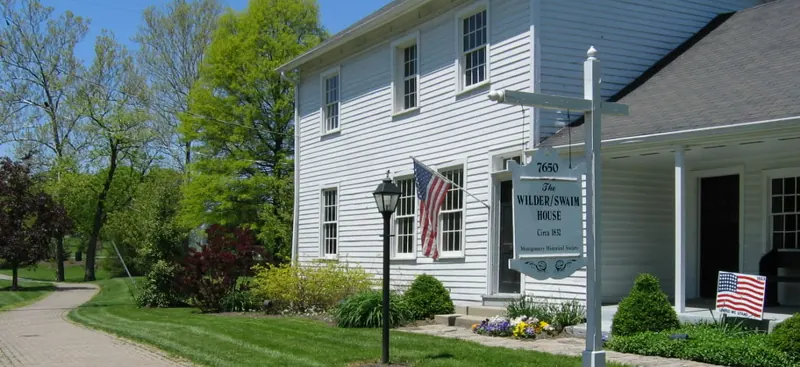 White clapboard Wilder-Swaim House with an American flag on a spring day in Montgomery